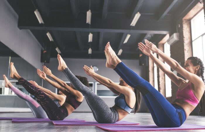 4 Frauen in Sportklamotten machen Pilatesübungen in einer Halle auf Matten